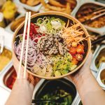 person holding brown wooden chopsticks with green vegetable salad