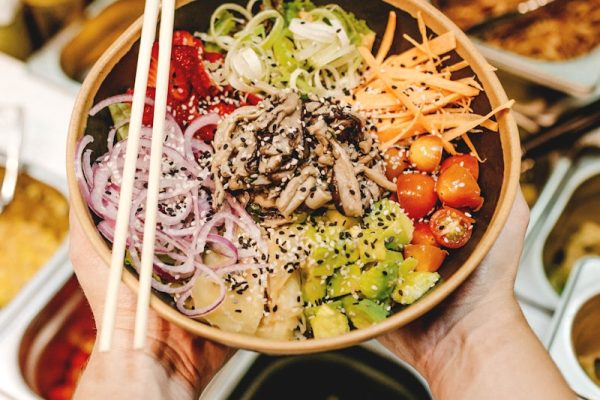 person holding brown wooden chopsticks with green vegetable salad