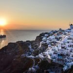 the sun is setting over a small village on a cliff