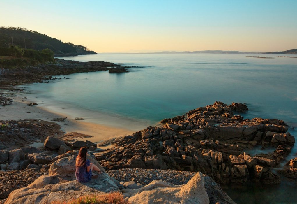 woman in blue and red dress sitting on rock near body of water during daytime