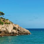 brown rocky mountain beside blue sea under blue sky during daytime