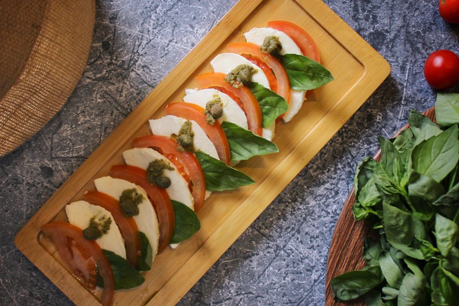 Mozzarella fresca con tomate y albahaca estilo caprese sobre tabla de madera