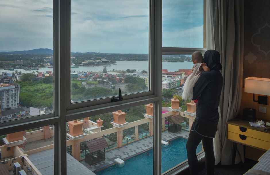Madre con su bebé mirando por la ventana de una habitación de hotel