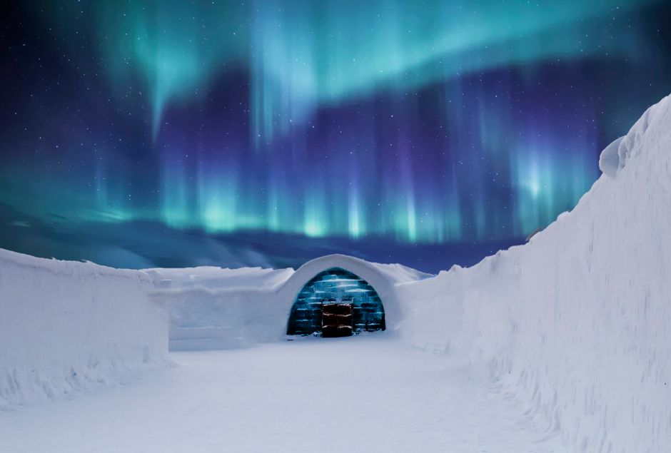 Aurora boreal sobre un iglú de cristal en un paisaje nevado del Ártico
